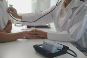 Jeune médecin est en utilisant une stéthoscope Ecoutez à le battement de coeur de le patient. coup de une femelle médecin donnant une Masculin patient une vérifier en haut photo