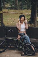 content Jeune asiatique femme tandis que équitation une vélo dans une ville parc. elle sourit en utilisant le vélo de transport. écologiquement amical concept. photo