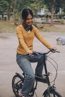 content Jeune asiatique femme tandis que équitation une vélo dans une ville parc. elle sourit en utilisant le vélo de transport. écologiquement amical concept. photo