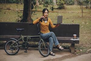 content Jeune asiatique femme tandis que équitation une vélo dans une ville parc. elle sourit en utilisant le vélo de transport. écologiquement amical concept. photo