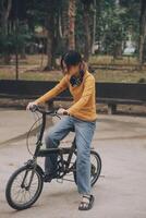 content Jeune asiatique femme tandis que équitation une vélo dans une ville parc. elle sourit en utilisant le vélo de transport. écologiquement amical concept. photo