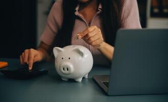 Jeune asiatique femme économie pour retraite économie argent par une porcin banque et prise Remarques sur carnet de notes, des économies concept. photo