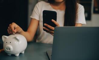 Jeune asiatique femme économie pour retraite économie argent par une porcin banque et prise Remarques sur carnet de notes, des économies concept. photo