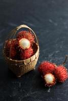 Frais ramboutan, été fruit dans une panier sur une noir Contexte photo