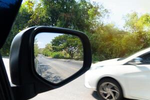 transport de voiture vue de miroir aile de auto. avec autre voiture conduite avec flanc vitesse. pouvez voir autre voiture drving loin cacher sur asphalte route. photo