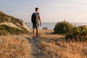 promeneur homme avec sac à dos randonnée sur le océan littoral avec montagnes et soir lumière du soleil. photo