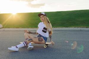 portrait de une branché Jeune fille souriant avec une longboard à le coucher du soleil. photo