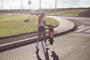 portrait de une branché Jeune fille souriant avec une longboard à le coucher du soleil. photo