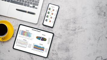 Haut vue de une moderne espace de travail avec une financier rapport affiché sur une tablette et téléphone intelligent, aux côtés de une portable et une tasse de café. photo