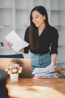 concentré femme d'affaires révision et organiser important les documents à sa bureau avec une portable et une vase de fleurs ajouter une personnel touche. photo