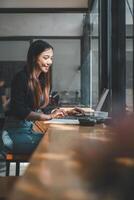 souriant femme d'affaires immergé dans sa travail sur une portable à une en bois table dans une confortable et ensoleillé moderne café. photo