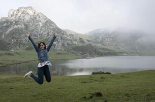 femme sauter pour joie dans de face de une Lac dans une montagneux paysage, dans des lacs de covadonga photo