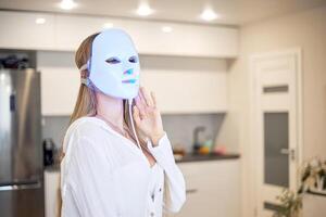 magnifique femme avoir une LED lumière thérapie masque traitement pour sa visage à maison. photo