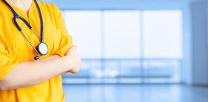 médical publicité. Jeune magnifique fille dans Jaune manteau avec stéthoscope et avec bras franchi hôpital. un impersonnel large Contexte. photo