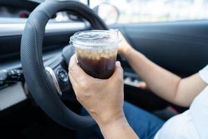 asiatique femme chauffeur en portant tasse pour boisson l'eau tandis que conduite une auto. Plastique chaud l'eau bouteille cause Feu. photo