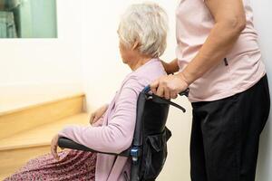 le soignant aide une vieille femme asiatique ou âgée assise en fauteuil roulant dans les escaliers à la maison. photo