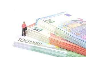 miniature homme d'affaire navigue le financier paysage, entouré par euro billets de banque, photo