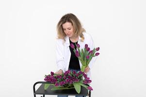 une mignonne fille collecté une bouquet de violet tulipes. des stands sur une blanc Contexte photo