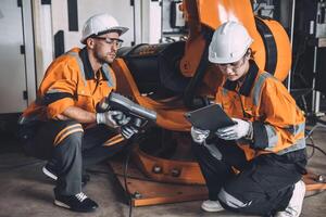 ingénieur équipe un service robot soudage travail dans automatisation usine. gens ouvrier dans sécurité costume travail robotique bras Logiciel programmation ou remplacer partie dans automatique fabrication industrie technologie. photo