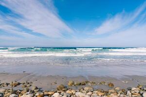 océan plage avec grand des pierres et le sable en dessous de une bleu ciel et des nuages photo