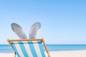 Pâques lapin oreilles relaxant sur une plage chaise par le mer photo