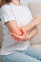 femme ayant coude mal pendant séance sur canapé à maison, muscle douleur dû à latéral épicondylite ou tennis coude. blessure, santé et médical concept photo