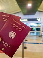 une main détient deux allemand passeports dans de face de une doux Voyage aéroport Contexte sur vacances. photo