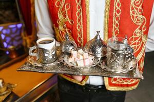 homme dans rouge et or tenue en portant plateau de argent thé et café photo