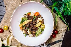 blanc bol rempli avec Viande et des légumes sur une en bois table photo