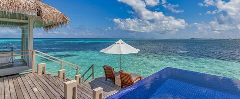 luxe plage station balnéaire, bungalow près interminable bassin plus de magnifique bleu mer. incroyable tropical île, été vacances concept. couple chaises avec parapluie, parfait été loisir vacances vacances panorama photo