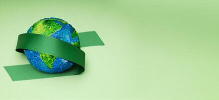 monde Terre journée concept. vert énergie, esg, renouvelable et durable ressources. environnement se soucier. vert ruban embrassement une globe. Haut vue photo