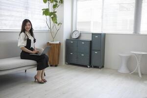 une Japonais femme vérification téléphone intelligent par éloigné travail dans le Accueil Bureau photo