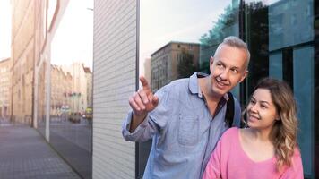 une aux cheveux gris homme dans une denim chemise est montrant quelque chose dans le distance à une Jeune femme. elles ou ils sont souriant. haute qualité photo