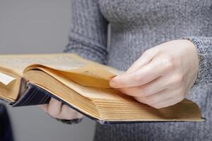 le main de un invisible la personne feuilles par le pages de un vieux et vieux livre. dans une Université ou école bibliothèque. haute qualité photo