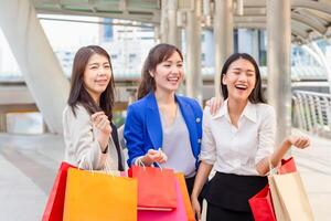 groupe de Jeune asiatique femmes porter achats Sacs tandis que en marchant le long de le rue. content la vie et achats concepts photo