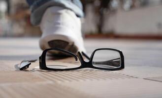 pied dans une blanc baskets fait un pas sur le lunettes. cassé verre sur rue carrelage . haute qualité photo