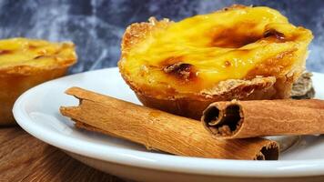 un pastel de nata ou Portugais Oeuf Tarte et cannelle des bâtons sur une blanc plaque. pastel de belme est une petit tarte avec une croustillant bouffée Pâtisserie croûte et une Crème crème remplissage. photo