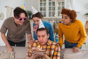 faire une souhait. homme portant fête casquette soufflant en dehors brûlant bougies sur anniversaire gâteau. content anniversaire faire la fête. groupe de copains vœux gars content anniversaire. gens célébrer anniversaire avec fête à Accueil photo