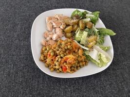 fait maison grillé poulet avec vert salade, pois Ragoût et concombre cornichons servi sur une blanc assiette photo