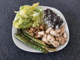 fait maison grillé poulet avec riz, vert salade et grillé asperges, servi sur une blanc plaque. brocoli des graines sur Haut de le riz photo