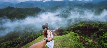 couple asiatique Voyage la nature. Voyage se détendre. content et profiter une magnifique la nature sur de pointe de brumeux Montagne. amoureux femmes et Hommes tenir mains fonctionnement sur le pelouse. sauvage la nature bois sur le Montagne. photo