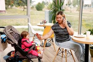 femme avec une enfant dans une poussette dans une café pourparlers sur le téléphone à le même temps divertit le enfant photo