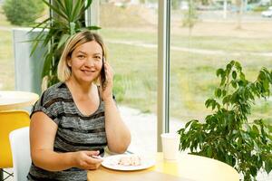 femme dans une café avec une sourire pourparlers sur le téléphone et mange dessert photo