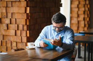 Sénior vieux homme en train de lire une livre dans une café boutique, profiter le sien littéraire loisir photo