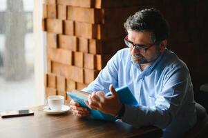 mature Beau homme en train de lire une livre dans une café photo