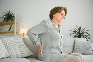 mature Dame séance sur lit et émouvant sa dos, radiculite et douleur photo