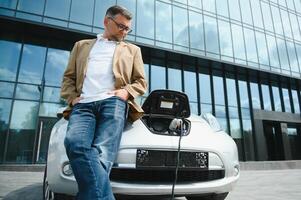 décontractée homme près électrique voiture attendre pour le terminer de le batterie mise en charge processus. photo