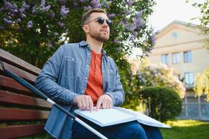 aveugle homme en train de lire braille livre, séance sur banc dans été parc, repos photo