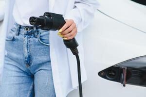 femme près de la voiture électrique. véhicule chargé à la borne de recharge. photo