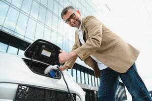 décontractée homme près électrique voiture attendre pour le terminer de le batterie mise en charge processus. photo